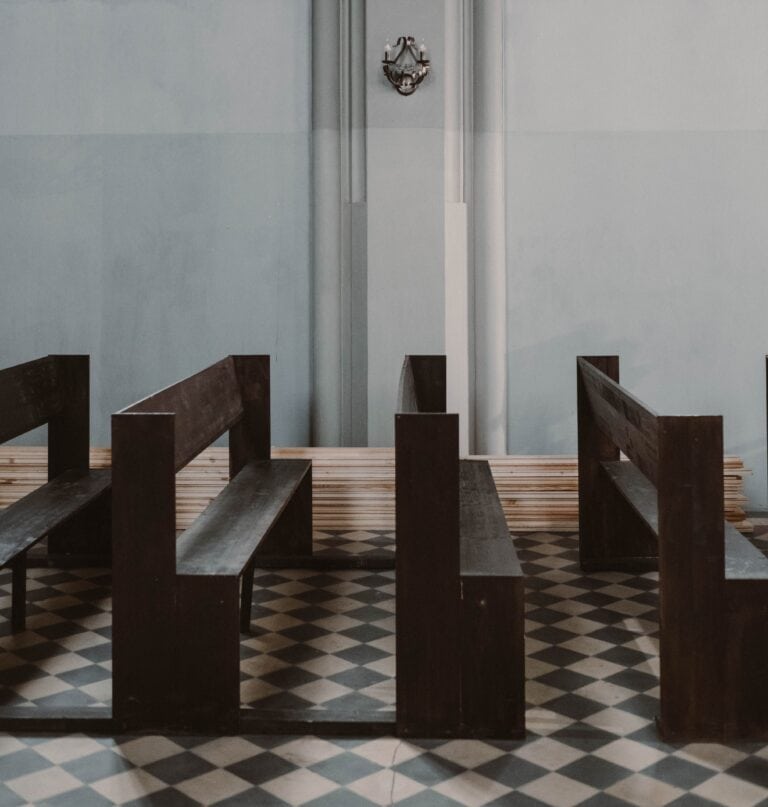Empty church pews with a patterned floor and a decorative wall ornament in a minimalist interior setting.